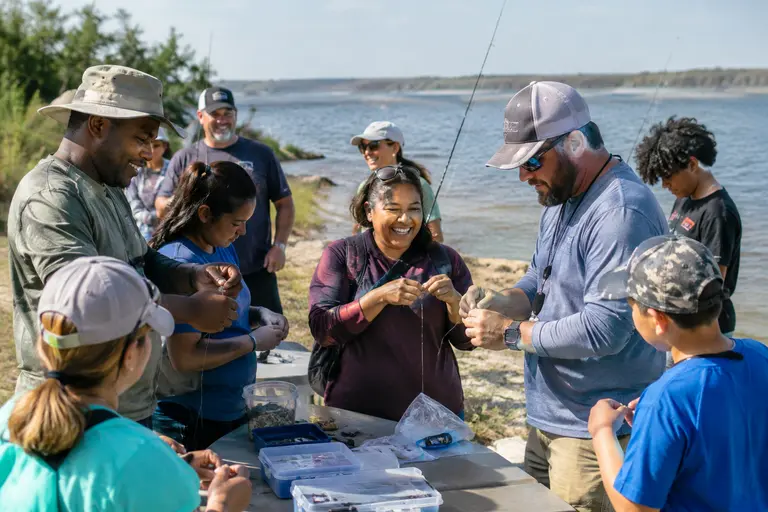 Families and volunteers stand near fishing gear during a park program